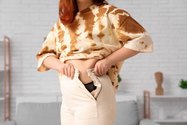 Image of woman trying to do her trousers up after pregnancy weight gain Kensington and Chelsea