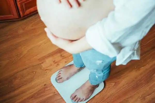 Image of woman weighing herself and experiencing weight gain through pregnancy Kensington and Chelsea